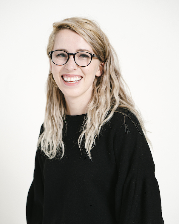 Picture of a smiling woman with long blond hair, black glasses, wearing a black sweater