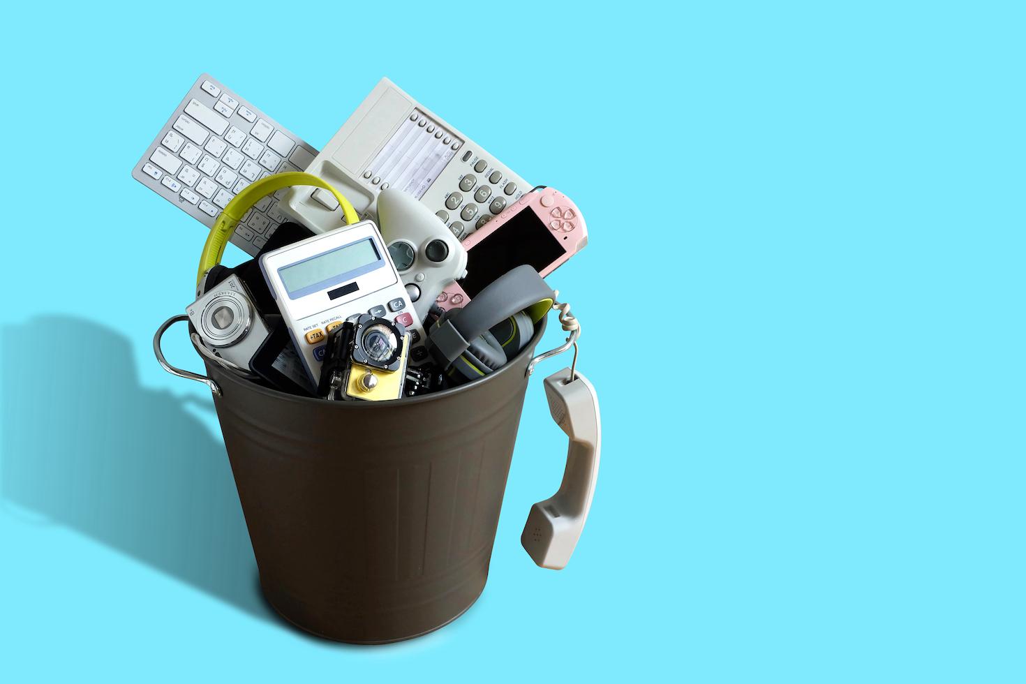 Graphic of phones, computer keyboards and other electronics devices heaped in a garbage bin.