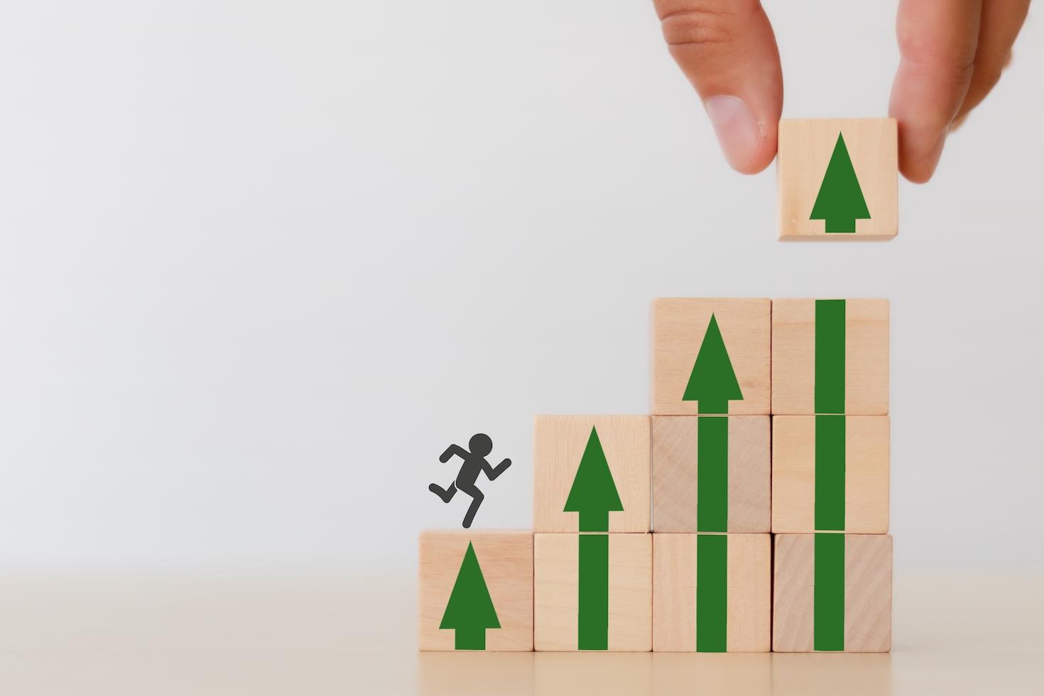 Stick figure climbing up stacked wooden blocks; upskilling, personal development concept