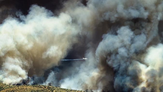  Aircraft flying through the dense white smoke rising from a raging wildfire