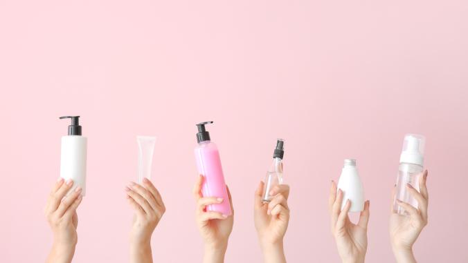 Hands holding different cosmetic products in bottles in front of pink background