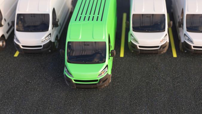 Row of several white vans with one green van in the middle parked slightly ahead of the others 
