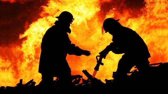 Silhouette of two fire fighters tackling a raging fire