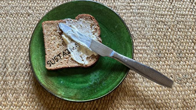 Dinner plate containing piece of bread with the word "sustainability" across it, smothered in part by mayonnaise