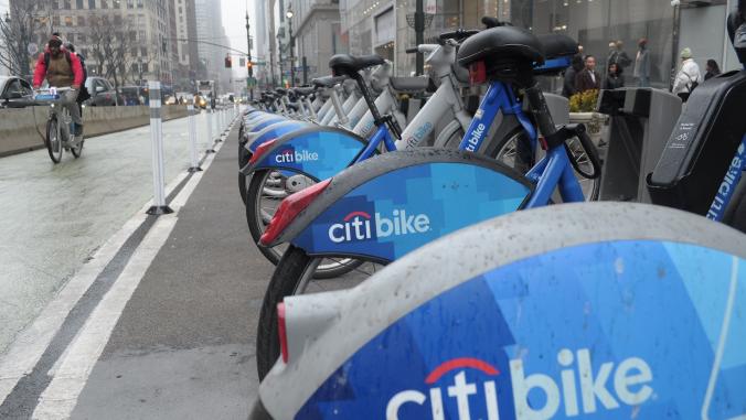 A cyclist rides a Citi Bike past a row of parked Citi Bikes down a street in Manhattan