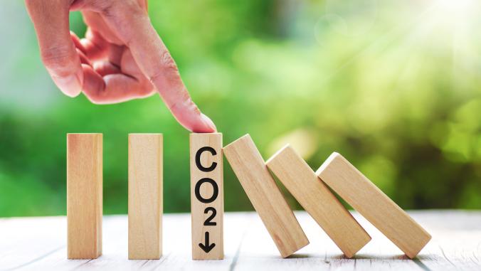 Several dominos, with a hand pointing to a domino labeled for lowering carbon dioxide