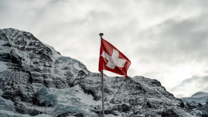 Swiss flag waving in the wind over snowy mountains under Alps cloudy sky